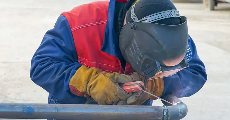 Un homme en combinaison bleu et rouge réalisant une soudure à l’arc électrique sur un tuyau