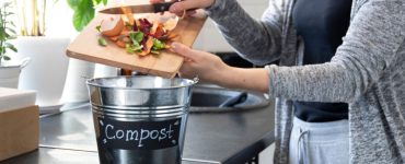 Une femme jette des boutures de légumes dans un seau à compost