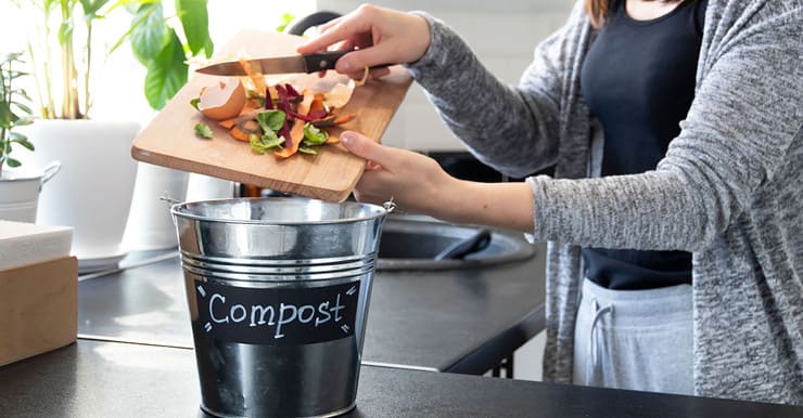 Une femme jette des boutures de légumes dans un seau à compost