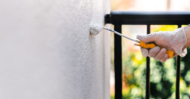 Focus sur la main d’une personne en gant blanc peignant le mur d’une terrasse avec un rouleau