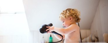 Un petit garçon dans la baignoire avec un sèche-cheveux dans les mains