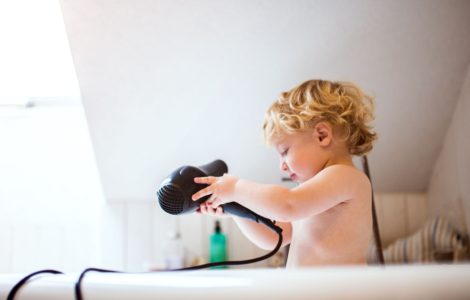 Un petit garçon dans la baignoire avec un sèche-cheveux dans les mains