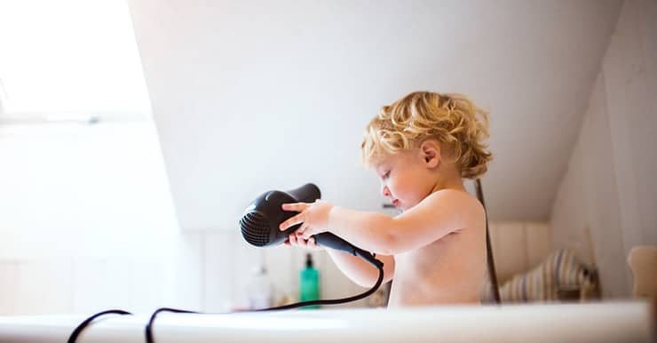 Un petit garçon dans la baignoire avec un sèche-cheveux dans les mains