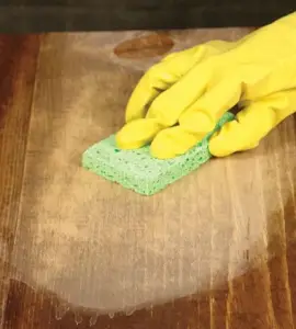 Zoom sur une main avec un gant jaune en train de frotter le parquet avec une éponge