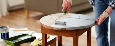 Une femme en gants peint une vieille table en bois à l’aide d’un rouleau de peinture