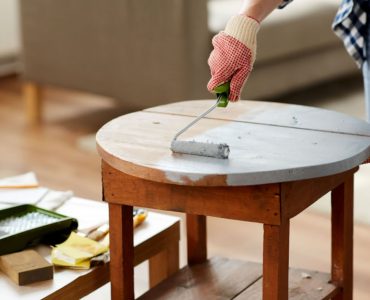 Une femme en gants peint une vieille table en bois à l’aide d’un rouleau de peinture