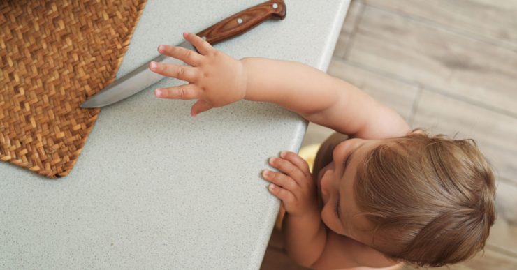 Un enfant essaie d'attraper un couteau posé sur le plan de travail de la cuisine