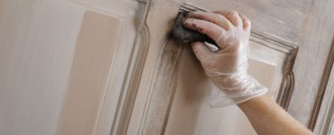 Gros plan sur la main d'une femme peignant une vieille porte en bois avec une patine marron
