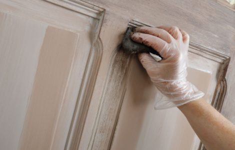 Gros plan sur la main d'une femme peignant une vieille porte en bois avec une patine marron