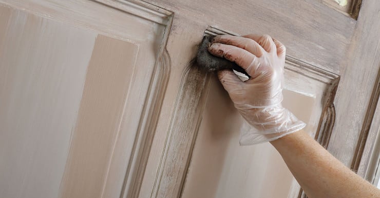 Gros plan sur la main d'une femme peignant une vieille porte en bois avec une patine marron