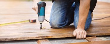 Un homme avec une perceuse électrique installe un parquet à l’extérieur