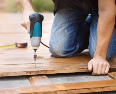 Un homme avec une perceuse électrique installe un parquet à l’extérieur