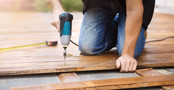 Un homme avec une perceuse électrique installe un parquet à l’extérieur