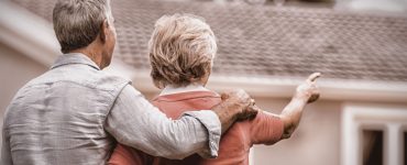 Un couple âgé en train de regarder leur maison en arrière plan