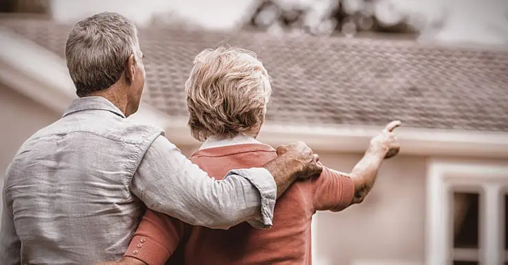 Un couple âgé en train de regarder leur maison en arrière plan