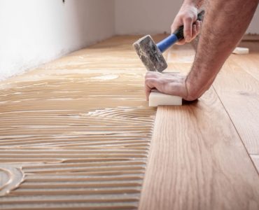 Un homme à genoux et tenant un marteau, en train de poser du parquet