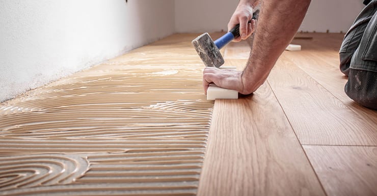 Un homme à genoux et tenant un marteau, en train de poser du parquet