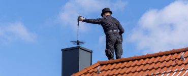 Un homme, debout sur le toit de la maison, effectue le ramonage d’une cheminée par le haut