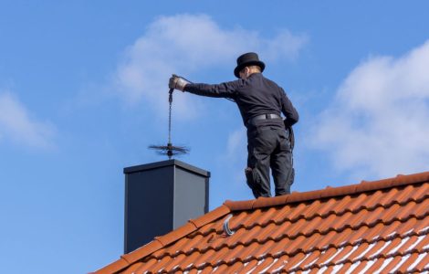 Un homme, debout sur le toit de la maison, effectue le ramonage d’une cheminée par le haut