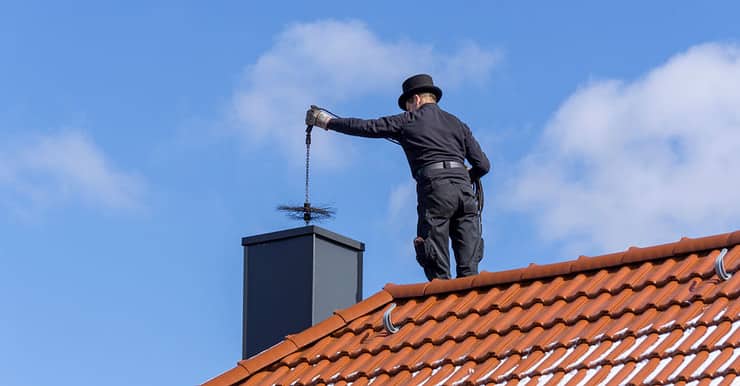 Un homme, debout sur le toit de la maison, effectue le ramonage d’une cheminée par le haut