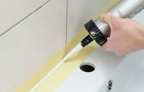 Zoom sur les mains d’un homme appliquant un joint en silicone dans la salle de bain