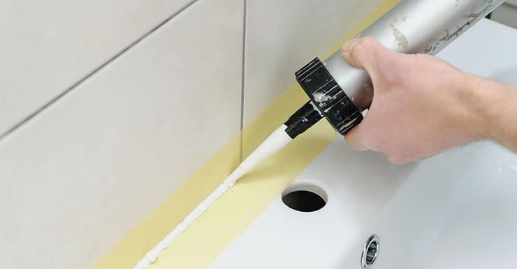 Zoom sur les mains d’un homme appliquant un joint en silicone dans la salle de bain