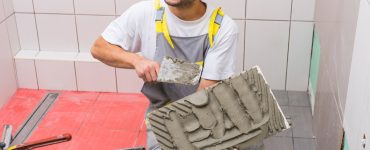 Un homme souriant pose un carrelage dans la salle de bains