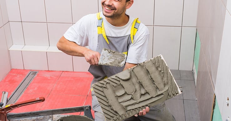 Un homme souriant pose un carrelage dans la salle de bains