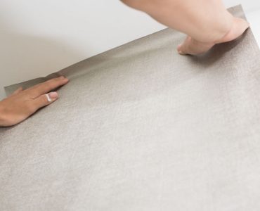Focus sur les mains d’un homme posant du papier peint sur le mur