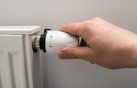 Main d'un homme tournant le robinet thermostatique d'un radiateur