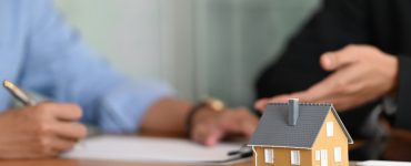 Une maquette de maison posée sur une table avec deux hommes en fond