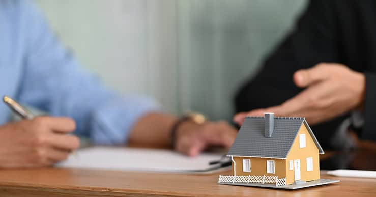 Une maquette de maison posée sur une table avec deux hommes en fond