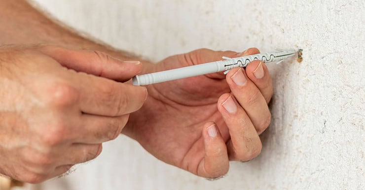 Zoom sur les mains d'un homme insérant une longue cheville en plastique dans le trou d'un mur