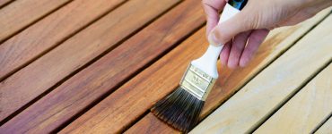 Focus sur la main d’une femme tenant un pinceau pour appliquer du vernis sur une surface en bois