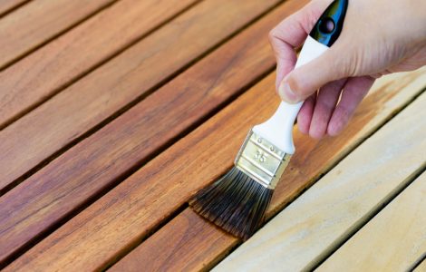 Focus sur la main d’une femme tenant un pinceau pour appliquer du vernis sur une surface en bois