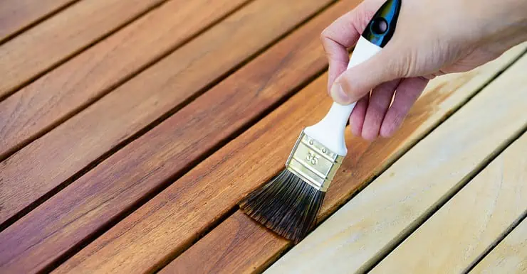 Focus sur la main d’une femme tenant un pinceau pour appliquer du vernis sur une surface en bois