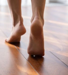 Une femme marche pieds nus sur la pointe des pieds dans une pièce en parquet