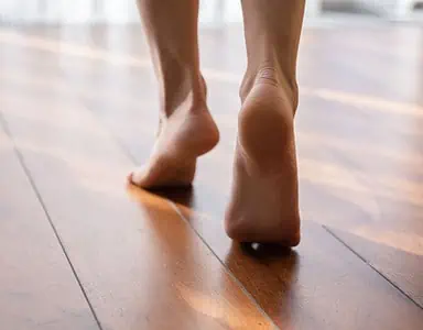 Une femme marche pieds nus sur la pointe des pieds dans une pièce en parquet