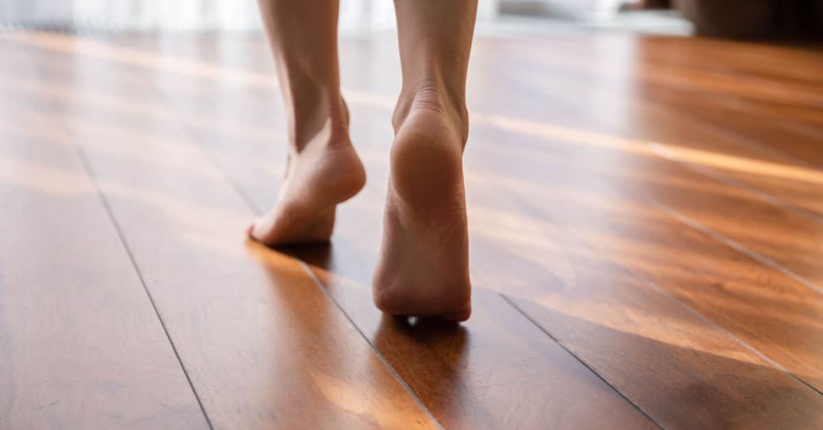 Une femme marche pieds nus sur la pointe des pieds dans une pièce en parquet