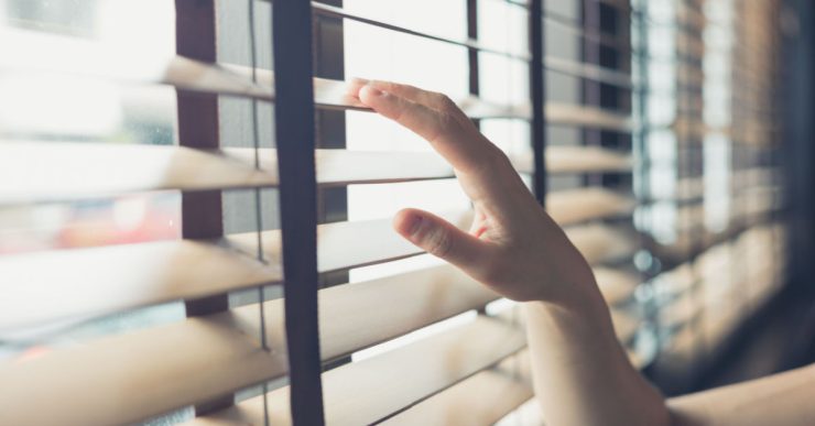 Une jeune femme touche les stores vénitiens d'une fenêtre