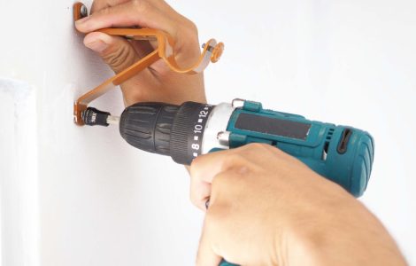 Zoom sur les mains d’un homme installant une tringle à rideau à l’aide d’une perceuse électrique