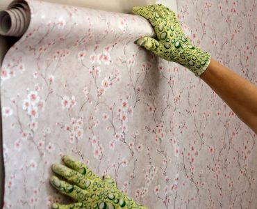 Focus sur les mains d’une femme avec des gants verts posant du papier peint avec des motifs fleuris