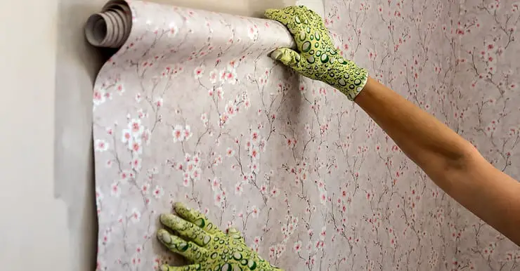 Focus sur les mains d’une femme avec des gants verts posant du papier peint avec des motifs fleuris