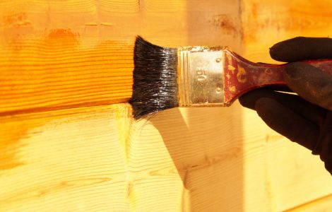 Zoom sur une main en gant en train de mettre du vernis sur un mur en bois