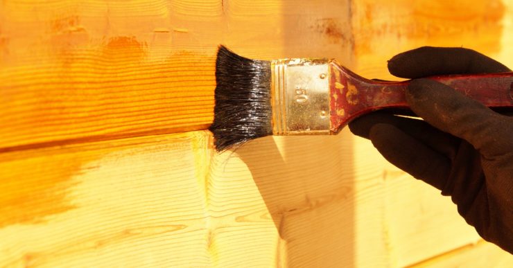 Zoom sur une main en gant en train de mettre du vernis sur un mur en bois