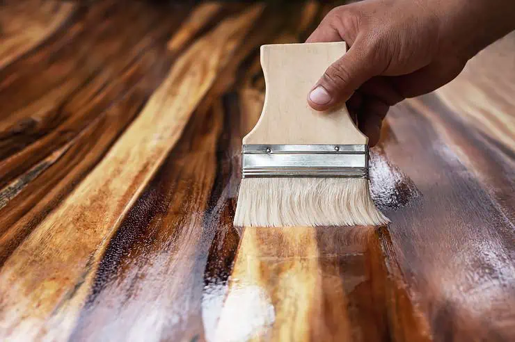 Focus sur la main d’un homme appliquant du vernis sur une surface en bois avec un pinceau