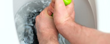 Focus sur les mains d'un homme débouchant les toilettes