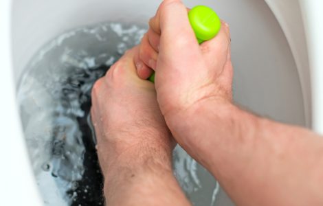 Focus sur les mains d'un homme débouchant les toilettes