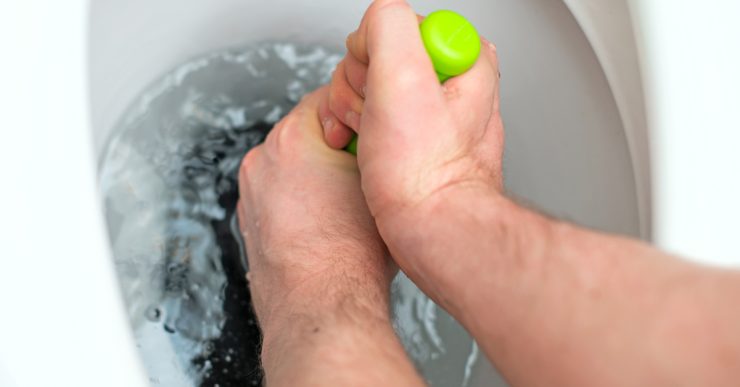 Focus sur les mains d'un homme débouchant les toilettes