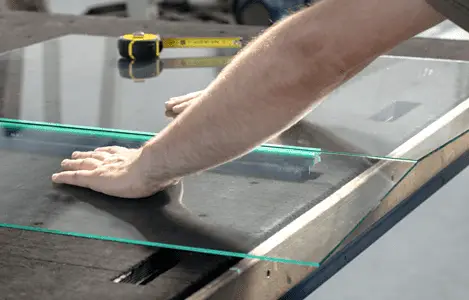 Zoom sur les mains d'un homme découpant du verre dans un atelier